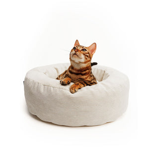 Bengalkatze liegt aufmerksam im cremefarbenen Katzenbett aus Cord – gemütlicher Rückzugsort für Katzen.