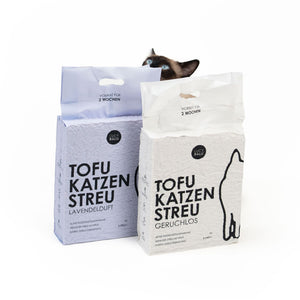 Zwei Beutel Tofu Katzenstreu nebeneinander, zwei Varianten: Geruchlos und Lavendel, Katze schaut von hinten darüber